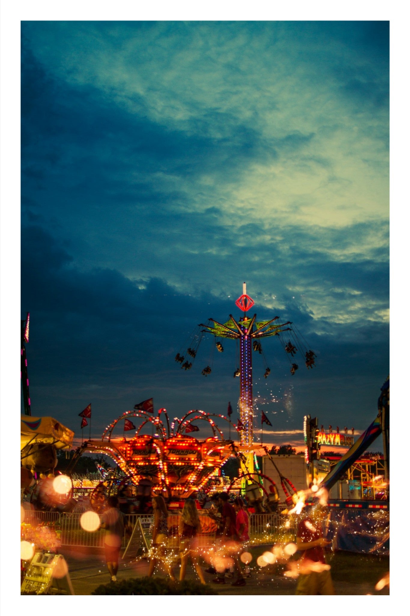 Abstract fine art photography of fairground ride lights, sparks and kinetic energy against a dark sky, industrial stillness, cinematic light architecture.