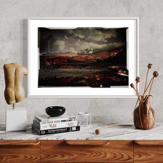 Framed artwork of a stadium at night on a wall above a wooden shelf with decor items.